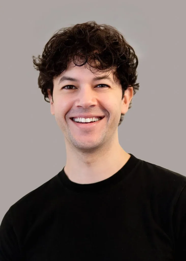 Adam, lead photographer in Paris, smiling in a black shirt against a neutral background.