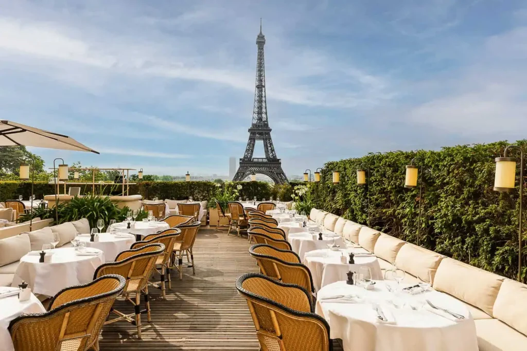 Girafe restaurant terrace at Trocadéro with rattan bistro chairs, white-clothed tables, and cream banquettes facing the Eiffel Tower