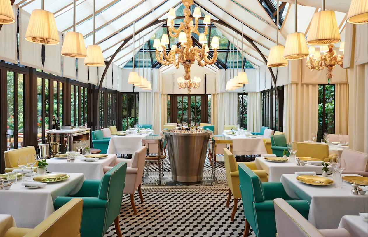 Il Carpaccio Paris restaurant bright conservatory dining room with teal and yellow armchairs, glass roof and Murano chandelier
