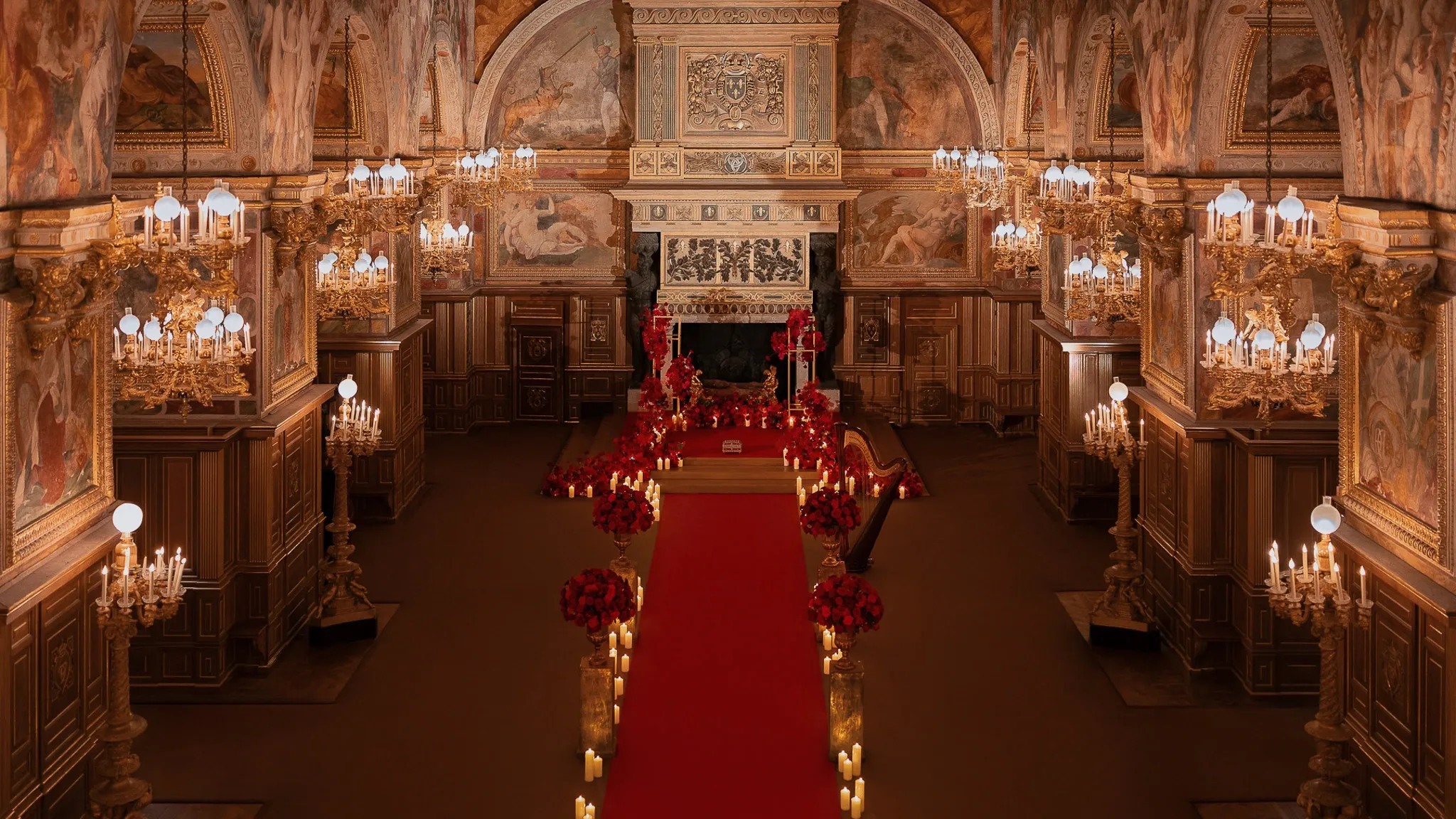 Private proposal setup inside Château de Fontainebleau ballroom — red carpet aisle, red rose installations, pillar candles, harp, and gilt chandeliers under frescoed ceilings