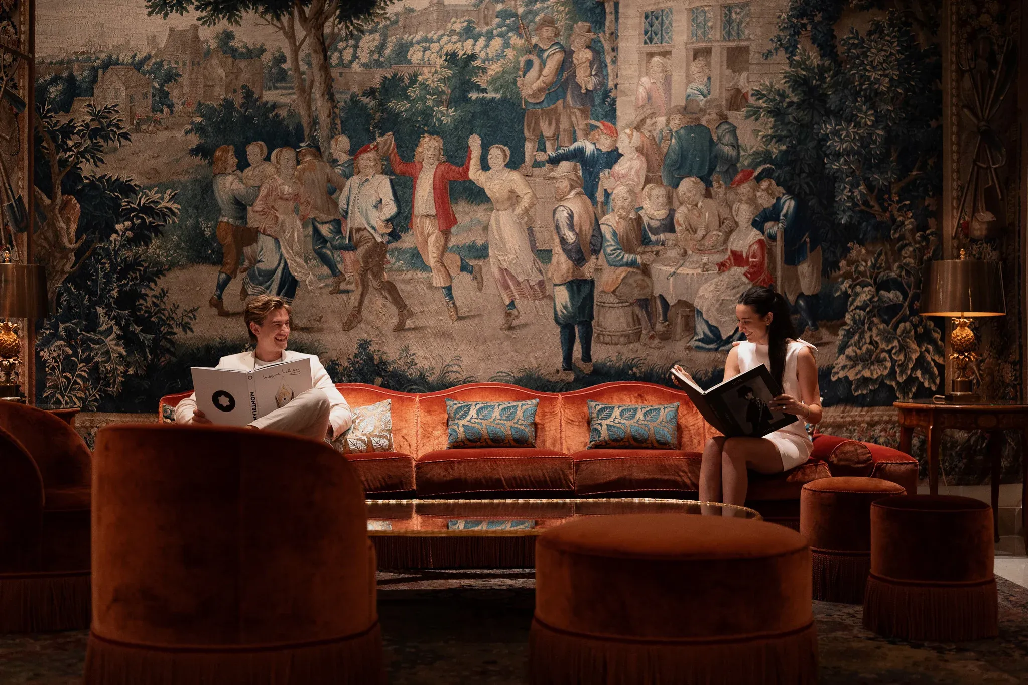 Couple relaxing on a burnt orange velvet sofa in front of a large Flemish tapestry in the grand lobby of Le Bristol Paris, luxury proposal venue produced by Kiss Me in Paris