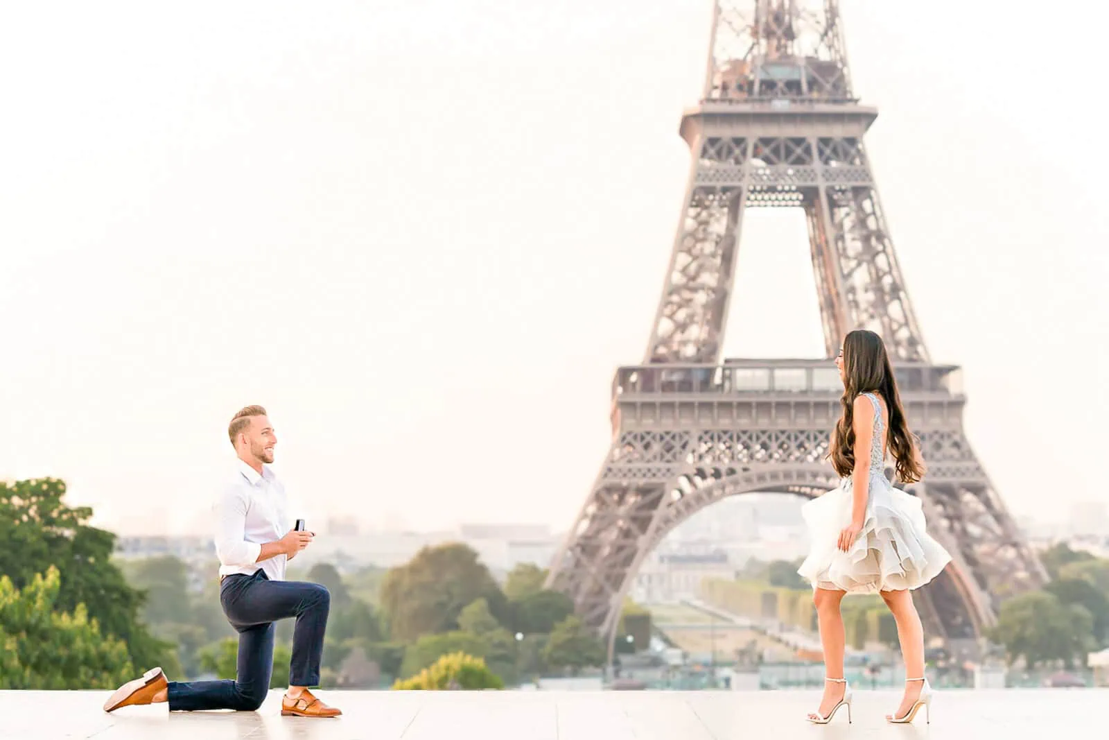 Surprise proposal at Trocadéro Paris at sunrise — man on one knee with ring box, Eiffel Tower directly behind, decoy photoshoot format