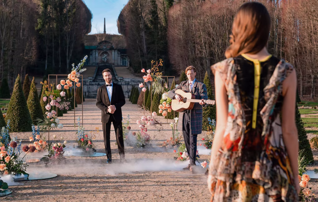 Proposal arrival at Château de Villette — man in tuxedo waiting at the end of a floral path with a live guitarist and ground smoke effects, Paris