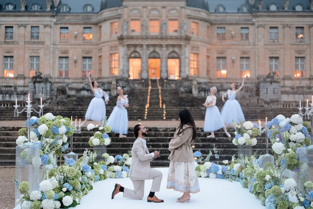 Proposal at Vaux-le-Vicomte château with live ballet performers on the grand staircase, blue and white hydrangea installations and candelabras on an overcast evening