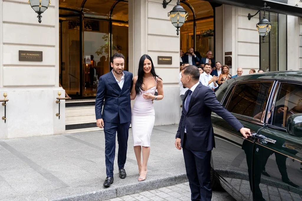 Newly engaged couple leaving The Peninsula Paris entrance to applause, with car door held open by staff