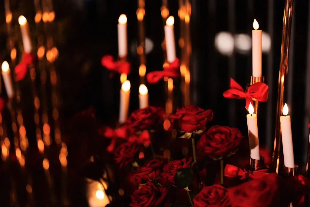 Close-up of red roses and white taper candles with red ribbon bows on gold candlestick holders, part of a luxury proposal setup in Paris at night