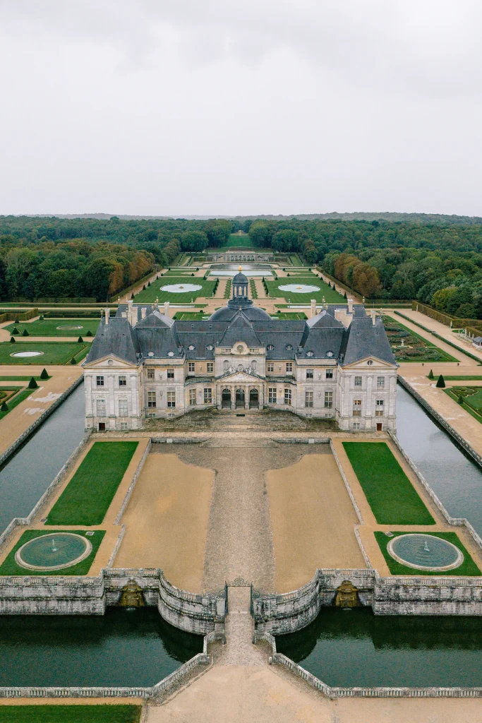 Aerial view of Château de Vaux-le-Vicomte with moat, formal gardens, and forest backdrop