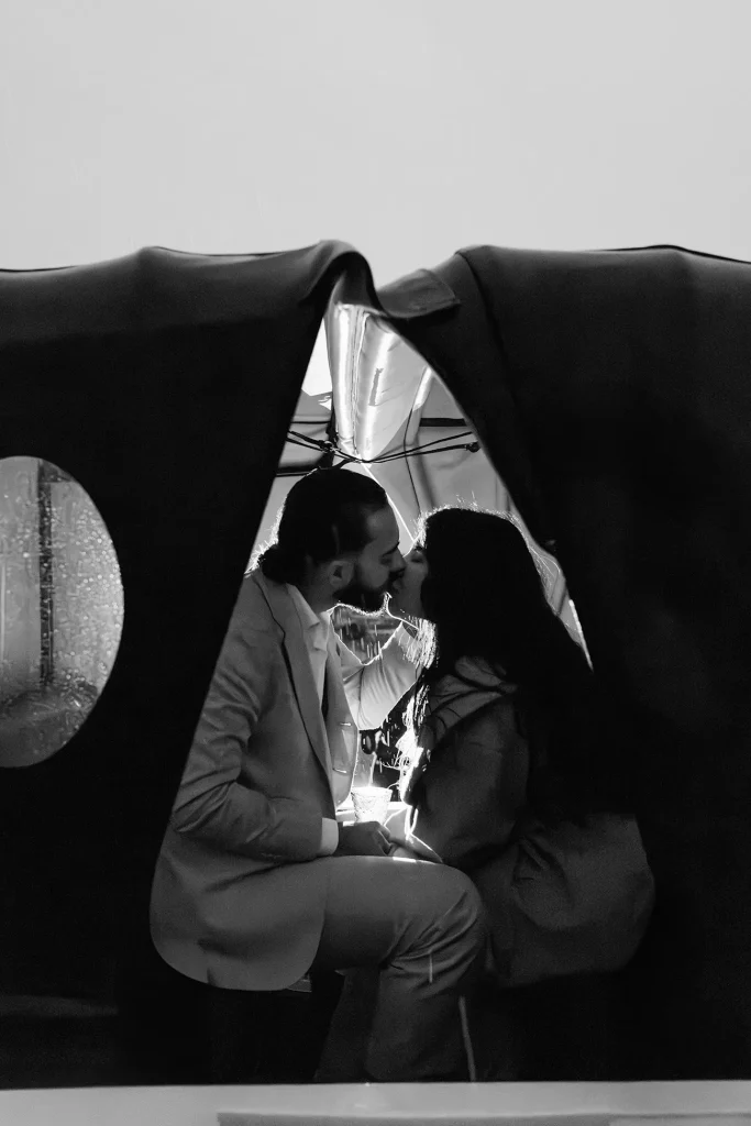 Black and white photo of couple kissing under the raised roof of a carriage in the rain
