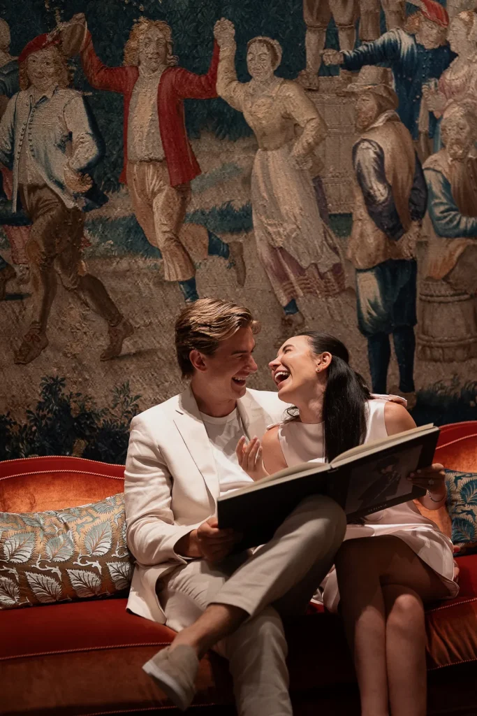 Ryan and Alexie laughing together on a sofa inside the Rambouillet Salon at Le Bristol Paris after their proposal.