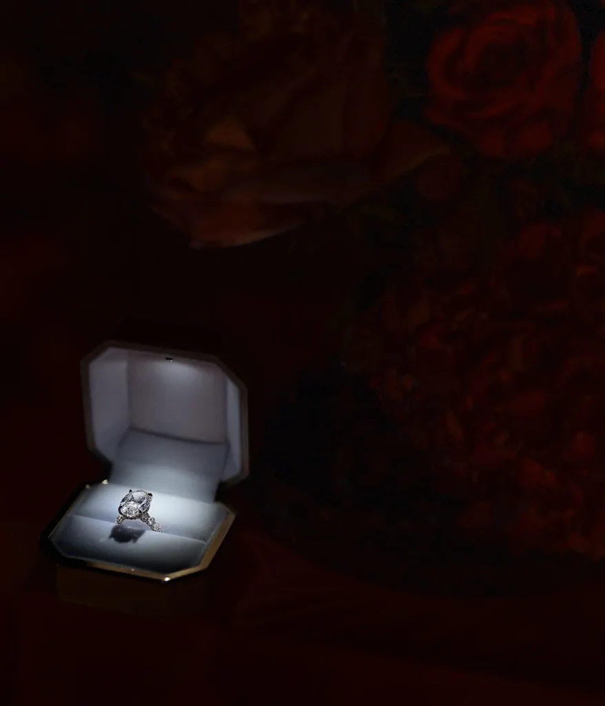 Open engagement ring box beside red roses before a private proposal at Château de Vaux-le-Vicomte.