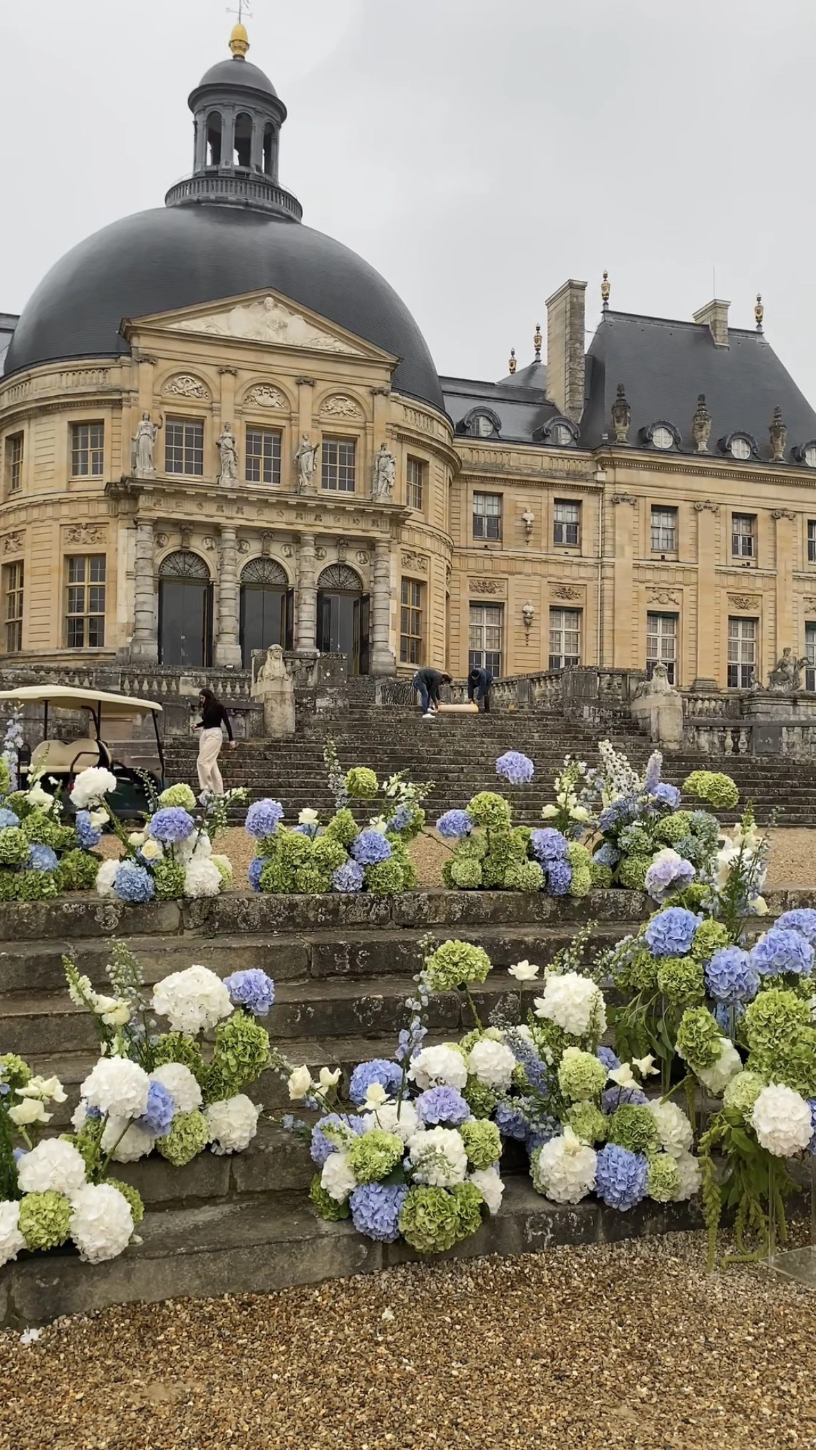 Blue and white hydrangea arrangements being placed along château staircase during daytime setup