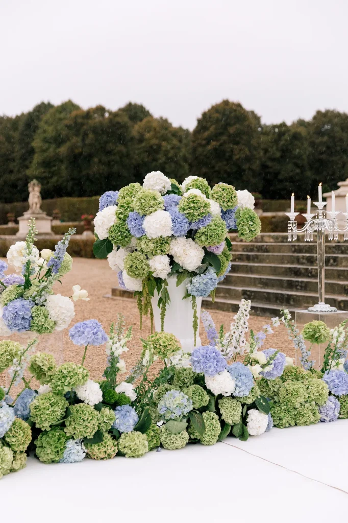 Close-up of blue, white, and green hydrangea arrangement in white urn along proposal aisle