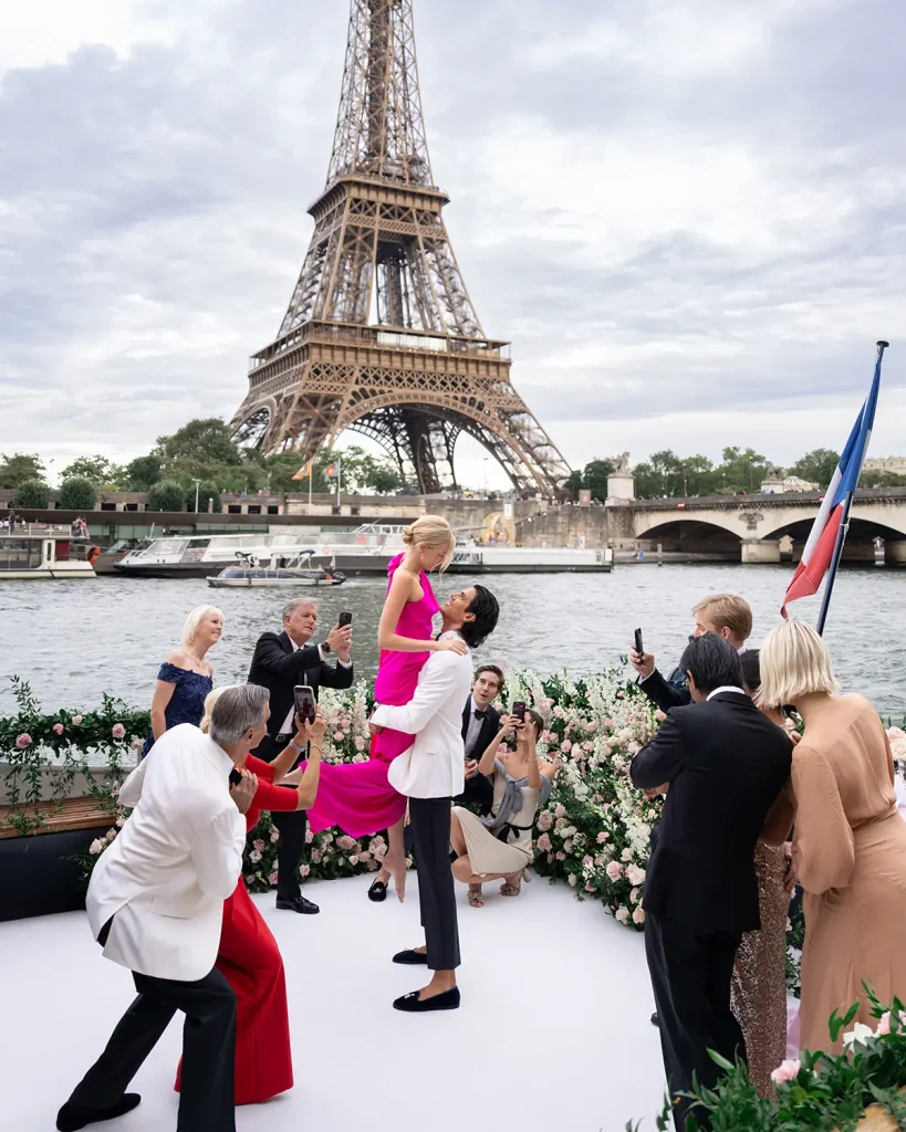 Newly engaged couple lifted and celebrated by family on a private Seine yacht with the Eiffel Tower behind them