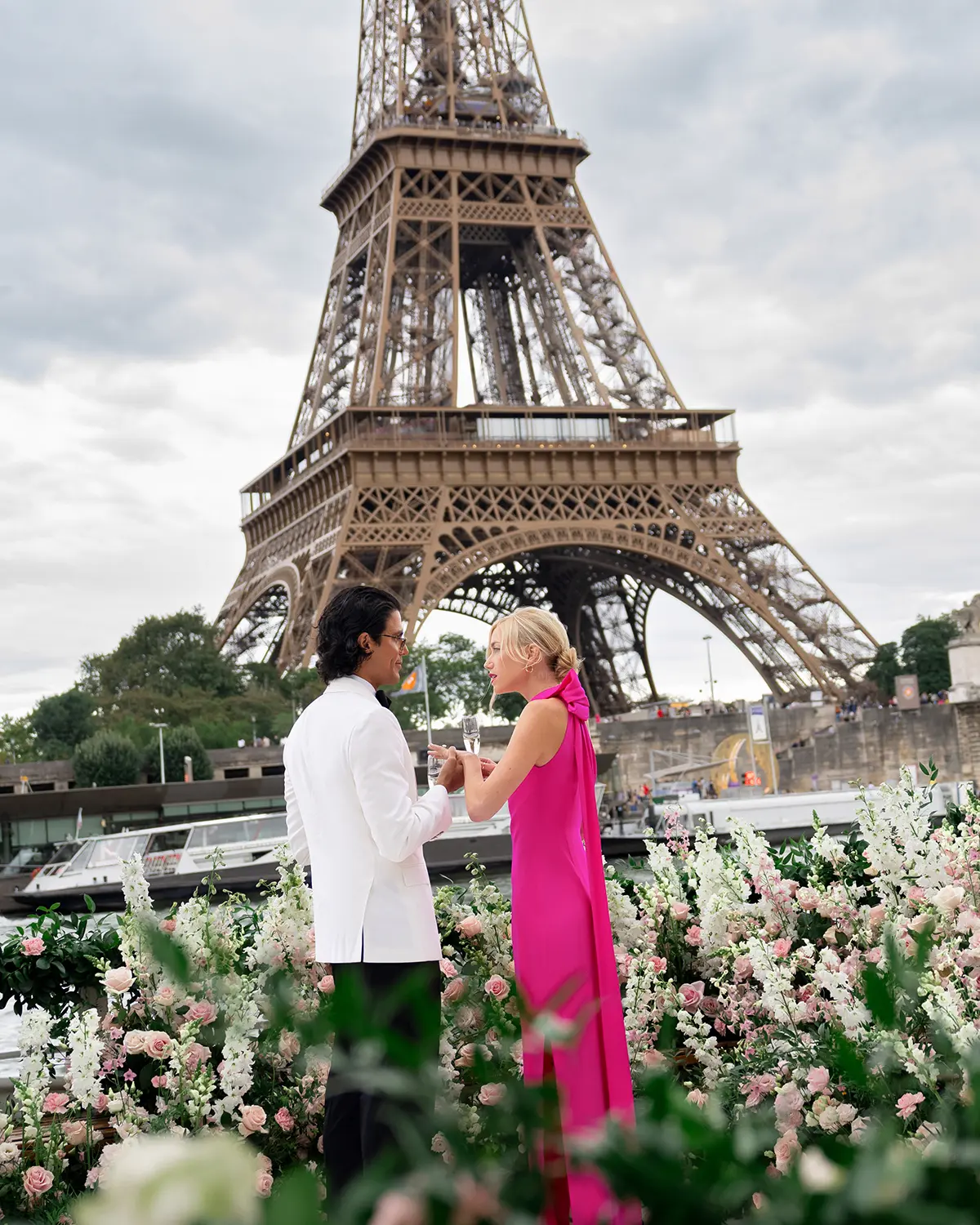 Newly engaged couple toasting with champagne on a private Seine yacht with the full Eiffel Tower behind them