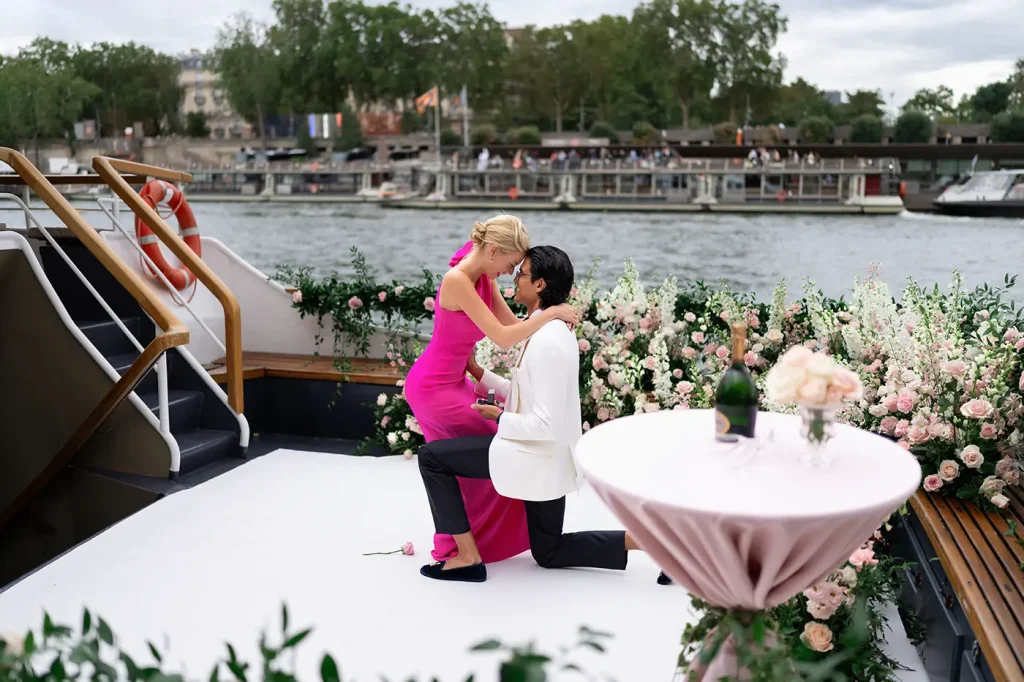 Man proposing on one knee with ring box on a private Seine yacht, woman leaning in toward him