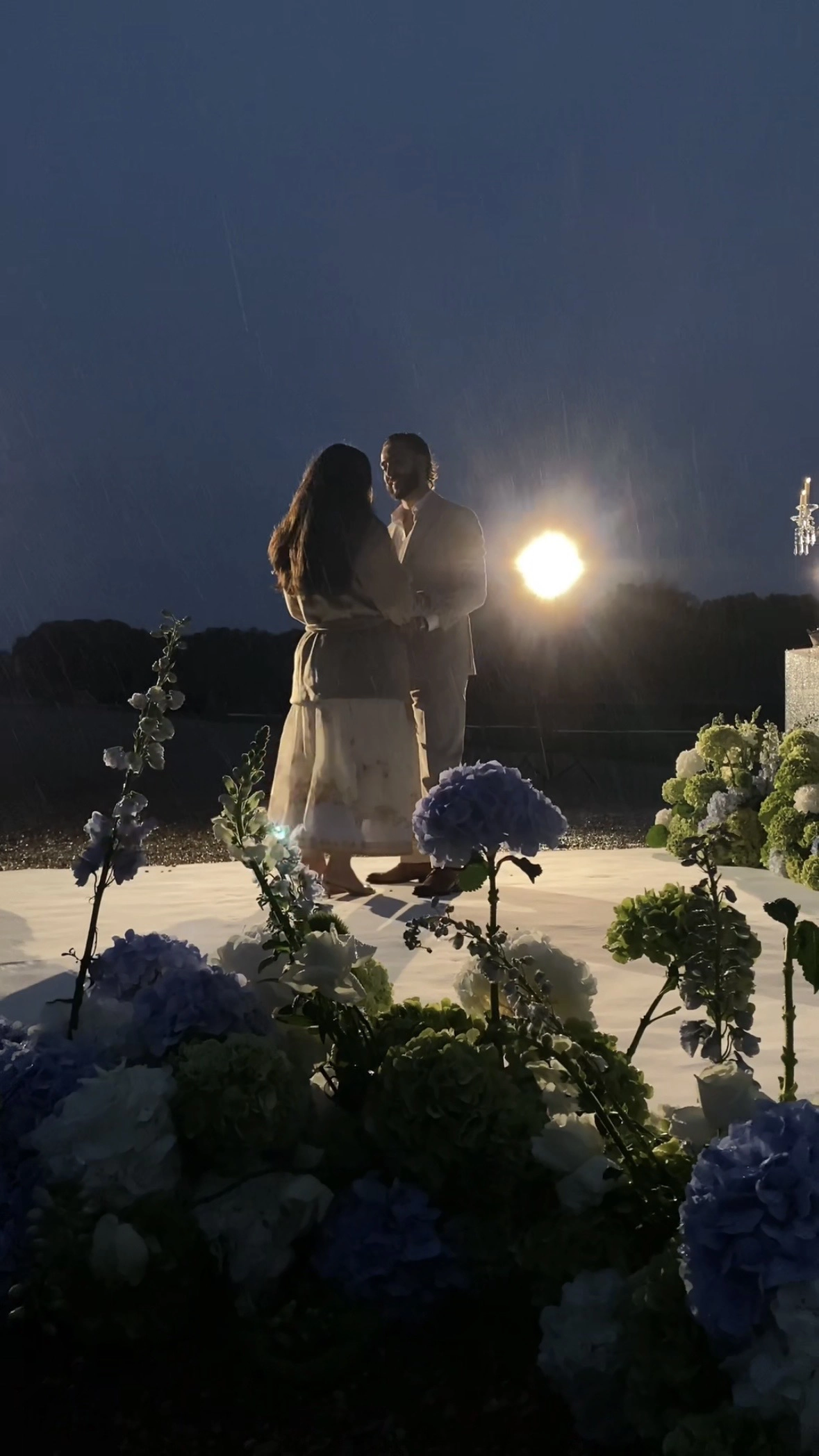 Couple embraces in silhouette during rain at nighttime proposal with hydrangea in foreground