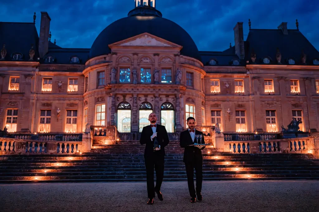 Staff bringing champagne down candlelit steps at Château de Vaux le Vicomte at night, proposal evening
