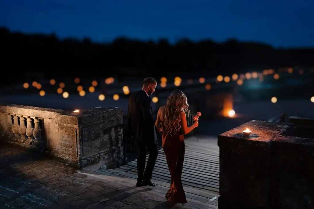 Couple walking a candlelit terrace at Château de Vaux le Vicomte at night, gardens lit with candles in the distance