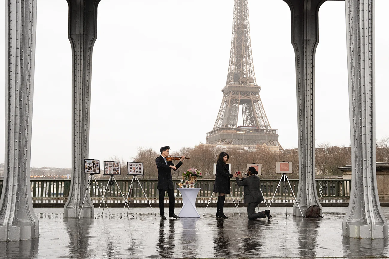 Man kneeling to propose under Bir-Hakeim bridge with the Eiffel Tower visible through the bridge's iron structure
