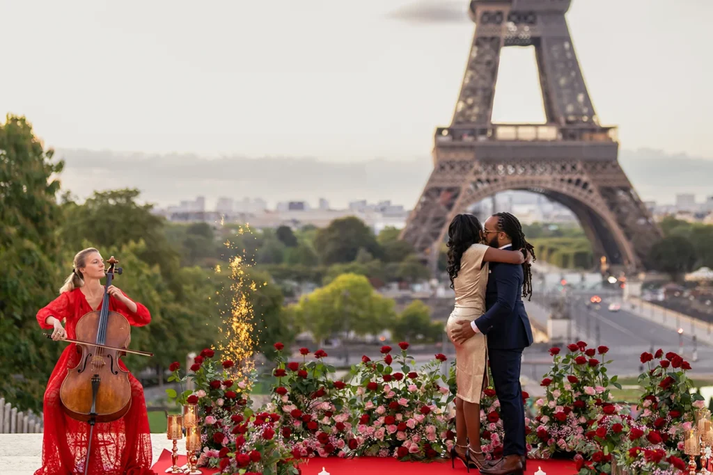 Couple embracing and kissing after a Trocadéro proposal with the Eiffel Tower behind them and a sparkler beside the rose-lined aisle