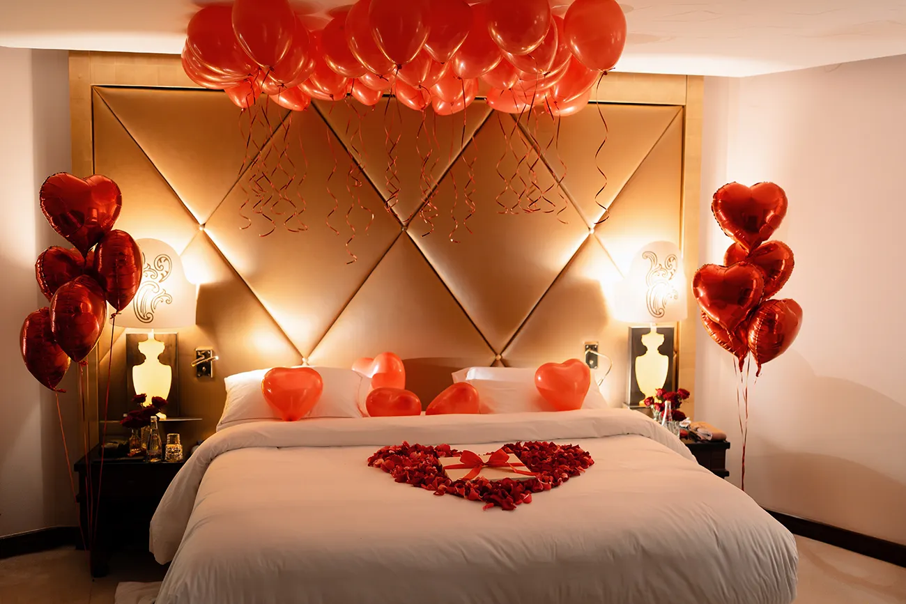 Hotel room decorated with red heart balloons and a heart shaped rose petal display on the bed at Le Bristol Paris