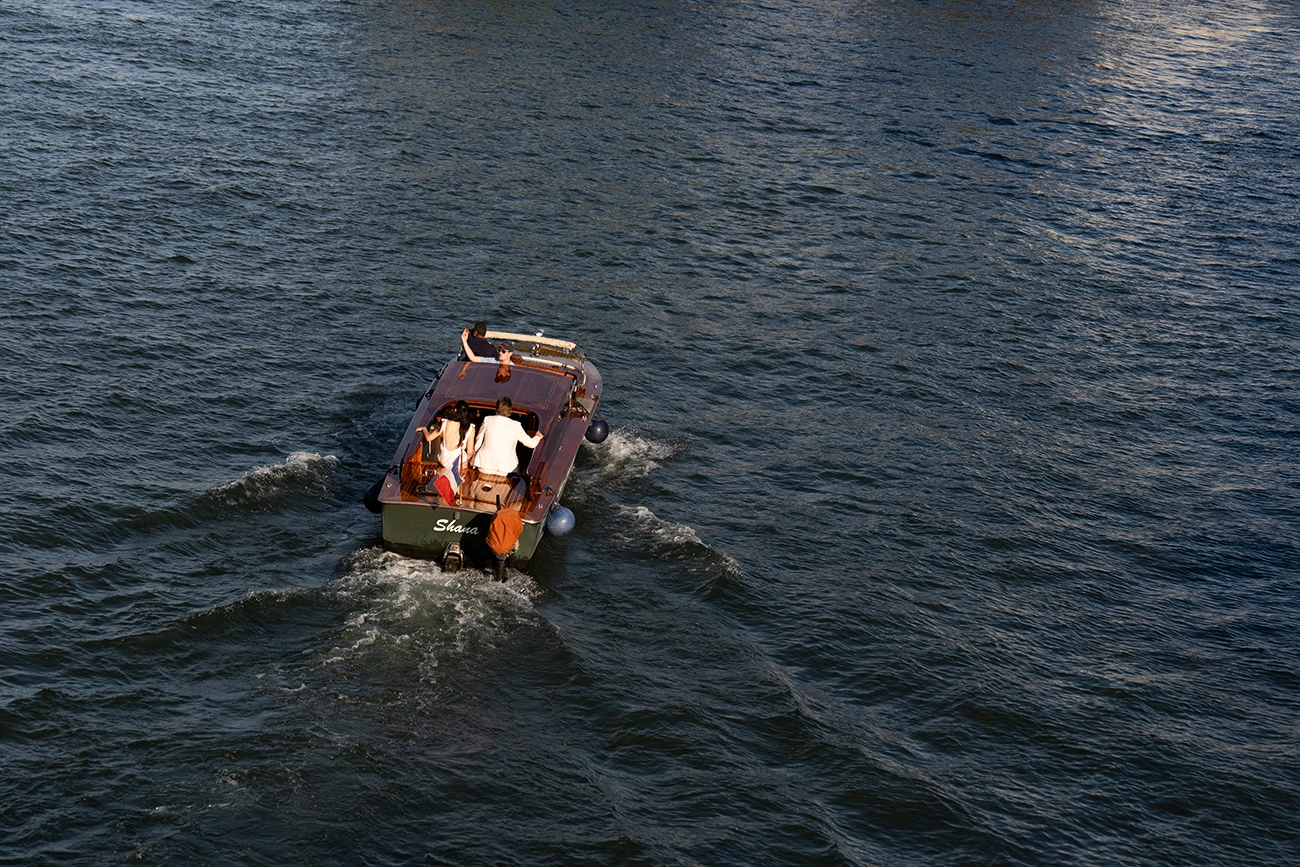 A small private motorboat carrying passengers travels across the Seine, leaving a wake behind it.