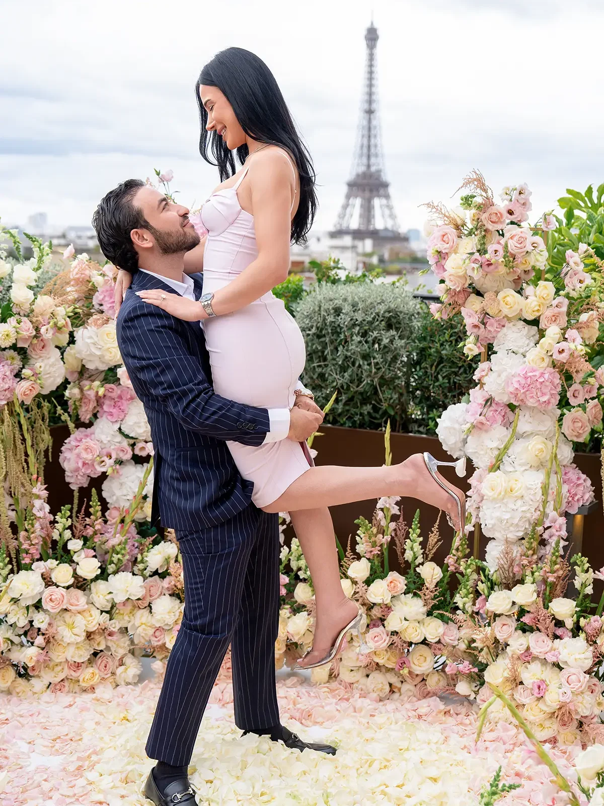 Man lifting his fiancée in celebration on The Peninsula Paris rooftop with Eiffel Tower in the background