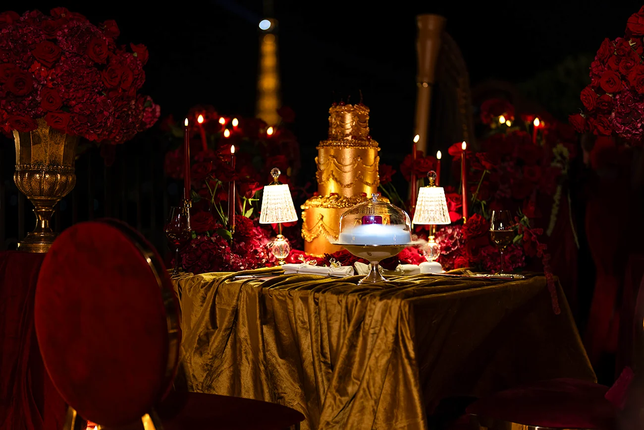 A private proposal dinner setting with red roses, candlelight, gold décor, and a tiered cake.