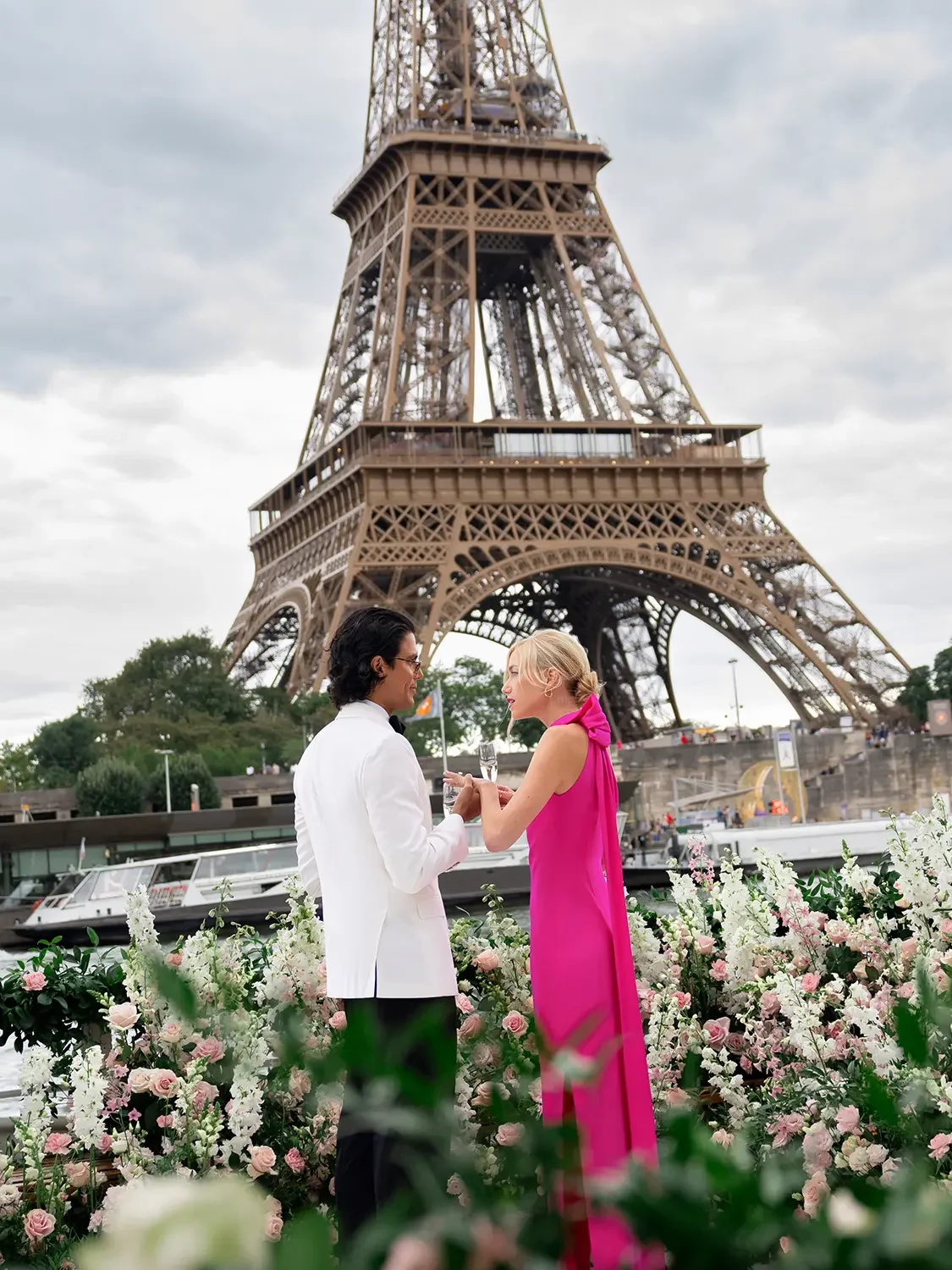 Newly engaged couple toasting with champagne on a private Seine yacht with the full Eiffel Tower behind them