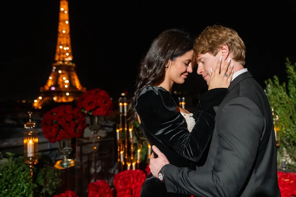 Couple embracing face to face at night with red roses and the Eiffel Tower behind them at Shangri La Paris